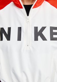 Balta puloverjakete ar sarkaniem akcentiem, ar ceturtā daļa rāvējslēdzis un liela melna "NIKE" logotipa priekšpusē. Gluda, viegla materiāla.