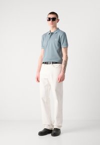 Lys blå polo skjorte med et lite logo, hvite bukser, svart belte, og svarte sko. Skjorten har klassisk krage og kontrastfarge.