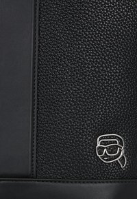 Black leather bag featuring textured surface and smooth accents, with a silver logo detail on the front.