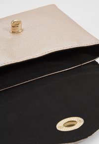 Borsa a pochette oro in materiale beige testurizzato, dotata di chiusura a scatto e fodera interna nera con dettaglio a ritaglio circolare.