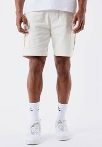 Pantalones cortos de carga para hombre en color crema con bolsillos laterales, detalles en amarillo contrastante, corte ajustado, material de algodón, combinados con calcetines blancos y zapatillas.}}
