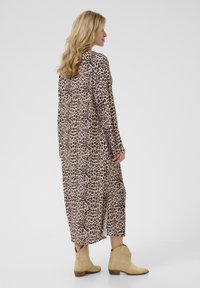 Rochie lungă cu imprimeu leopard, confecționată dintr-un material ușor, cu mâneci lungi și tiv despicat, asortată cu botine beje. 