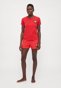 Maglietta rossa in cotone con maniche corte e logo di un orso sul petto, abbinata a pantaloni corti rossi in cotone con logo di un orso.