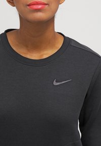 Sudadera negra de Nike con cuello redondo, textura suave y un sutil logo en forma de swoosh gris en la parte superior izquierda.