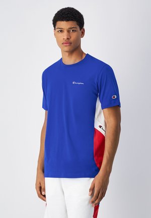Royal blue T-shirt featuring the Champion logo on the chest. Side panels in white and red create a color-blocked effect. Short sleeves.