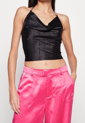 Crop top in satin nero con scollo drappeggiato e texture a motivi; abbinato a pantaloni in seta rosa brillante con tasche laterali e passanti per cintura.