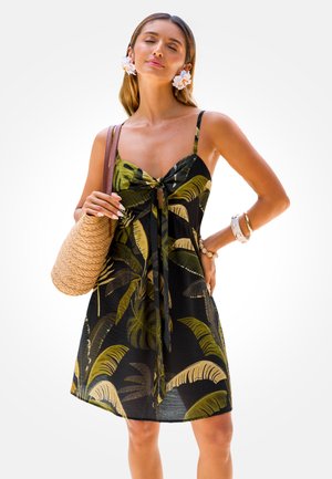 Vestido negro con estampado de hojas tropicales verdes, con lazo delantero y tirantes finos. Acompañado de un bolso tejido y pulseras.