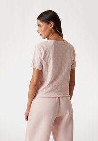 Pink short-sleeved t-shirt made of soft material, featuring a subtle all-over logo pattern, round neck, and relaxed fit.