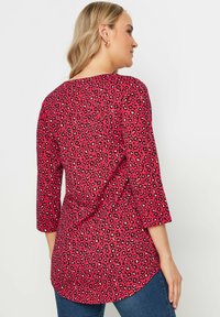 Top rosso con maniche a tre quarti caratterizzato da un motivo a stampa leopardata nera. Il tessuto appare liscio con un orlo arrotondato e una vestibilità morbida.