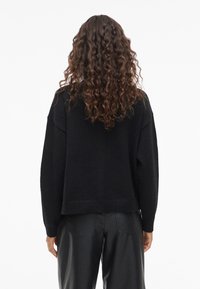 Svart kortad tröja i mjukt material med sänkta axlar och ribbad fåll, kombinerad med svarta läderbyxor.