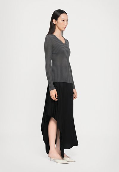 Grey ribbed long-sleeve top with a V-neck, paired with a black asymmetrical wrap skirt and white mules with pointed toes.