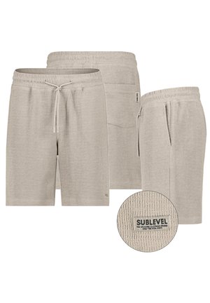 Beige gestrickte Shorts mit Kordelzug, vorderen und hinteren Taschen sowie einem strukturierten Stoffetikett mit der Aufschrift "Sublevel" auf der Gesäßtasche.