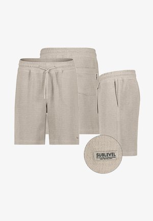 Beige gestrickte Shorts mit Kordelzug, vorderen und hinteren Taschen sowie einem strukturierten Stoffetikett mit der Aufschrift "Sublevel" auf der Gesäßtasche.