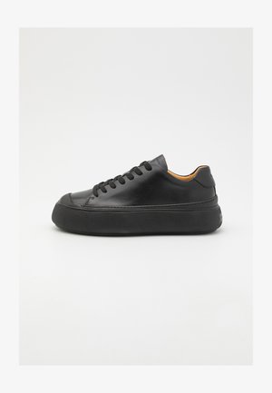 Black leather sneaker with a round toe, lace-up front, smooth texture, thick rubber sole, and contrasting tan interior.