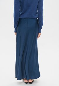 Garšīgs, plūstošs tumši zils svārks no mīksta auduma, ar gludu tekstūru un plašu apmalēm, kombinēts ar pieguļošu zilu džemperi.