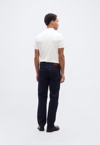 Λευκό πόλο με κοντά μανίκια συνδυασμένο με σκούρο μπλε τζιν παντελόνι. Το τζιν έχει πίσω τσέπες και καφέ δερμάτινη ετικέτα στη μέση.