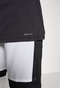 Maglietta sportiva nera Dri-FIT con orlo e testo grigio; abbinata a pantaloni corti bianchi e neri con dettagli a coste e pannelli laterali.