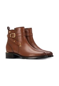 Botas de tobillo de cuero marrón con una textura suave, correa lateral con hebilla y tacón bajo en bloque. Incluye una lengüeta en la parte trasera para facilitar su colocación.