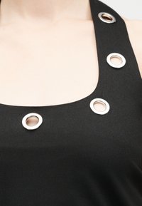 Μαύρο αμάνικο τοπ με φαρδιές τιράντες που διαθέτουν τρία μεγάλα ασημένια μεταλλικά ρούχαγα σε μία τιράντα και στο ντεκολτέ.