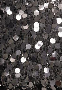 Schwarzer Stoff, bedeckt mit verschiedenen runden Pailletten in Silber- und Grautönen, unterschiedlich groß und lichtreflektierend, was eine strukturierte Oberfläche erzeugt.