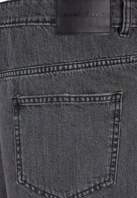 Grå denimjeans med en baglomme og et sort lædermærke fastgjort til taljebåndet. Stofstrukturen ser lidt falmet ud.