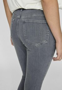 Vaqueros ajustados de mezclilla gris con una cintura de tiro medio, dos bolsillos traseros y una textura suave, que muestran una silueta ajustada.