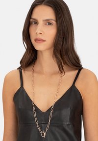 Sort lædertop med tynde stropper og V-udskæring, prydet med en guld kæde med aflange led og en circular accent.