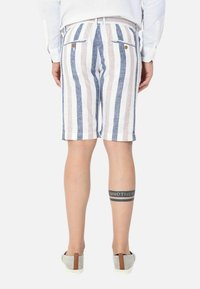 Pantaloni corti in lino con strisce verticali blu e beige, due tasche posteriori e cintura elastica. Indossati con scarpe grigie.