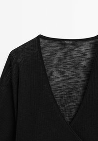 Schwarzes Strickoberteil mit tiefem V-Ausschnitt, aus leichtem, strukturiertem Stoff mit dezenter Transparenz. Das Etikett trägt die Aufschrift "Massimo Dutti".