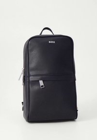 Juodos odos kuprinė su lygiu paviršiumi, turinti priekinę kišenę, sidabrinę užtrauktuką, logotipą viršuje ir viršutinę rankeną nešimui.