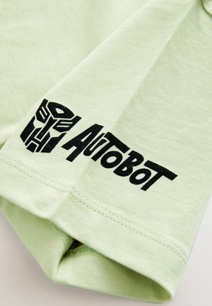 Šviesiai žalia medvilninė marškinėliai su juodu "Autobot" tekstu ir logotipu, atspausdintu ant rankovės. Trumpomis rankovėmis ir laisvu siluetu.