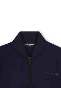 Veste bomber bleu marine avec col côtelé, fermeture éclair centrale noire et "Karl Lagerfeld" brodé sur la poitrine.