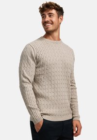 Lys beige genser med ripet tekstur, rund hals og lange ermer. Laget av et mykt, strikket stoff, med subtile vertikale mønstre.