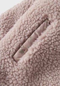Soft pink fleece fabric with a textured surface, featuring a floral-patterned inner layer visible through a slit detail.