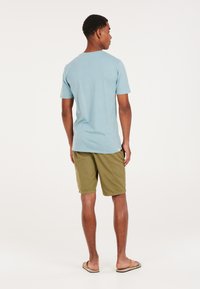 Camiseta de manga corta de color azul claro combinada con pantalones cortos de color verde oliva. La camiseta está hecha de un material suave y tiene un corte relajado; los pantalones cortos son hasta la rodilla.