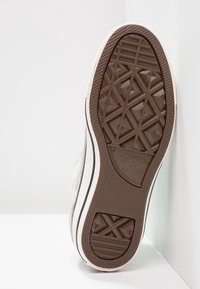 Podeszwa białego trampka Converse All Star z brązowym gumowym bieżnikiem o geometrycznych wzorach i logo, na tle białego tła z krawędziami.