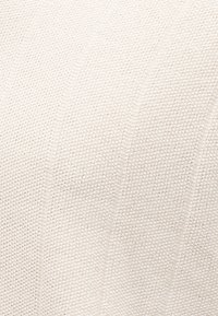 Υφασμα σε κρεμ απόχρωση με υφή και πλεκτό μοτίβο, που παρουσιάζει μικρές, ομοιόμορφες θηλιές δημιουργώντας μια απαλή, πυκνή επιφάνεια.