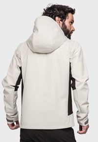 Light beige waterproof jacket with a large hood, dark brown accents, and elastic cuffs. Features a smooth texture and fitted design.