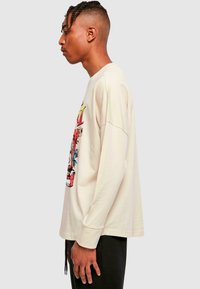 Cream long-sleeve T-shirt featuring a colorful graphic print on the front. Soft material with a relaxed fit and dropped shoulders.