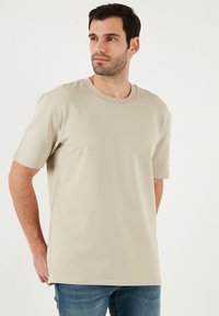 Světle béžové tričko s krátkým rukávem vyrobené z hladkého bavlněného materiálu s kulatým výstřihem. Volný střih, minimální švy a měkká textura.