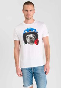 Camiseta de algodón blanca con un gráfico de un perro en un casco azul con estrellas blancas y una rosa roja en la boca. Corte casual con mangas cortas.