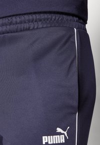 Jūriniai sportiniai kelnės, pagamintos iš lygaus audinio, su baltais šonais ir logotipu. Elastingas juosmuo užtikrina patogumą ir gerą prigludimą.