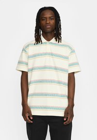 Korte mouwen polo shirt in crème met horizontale strepen in blauw, rood en geel. Beschikt over een geknoopte kraag en een gestructureerde stof.