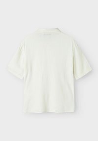 Kortärmad skjorta i ljus krämfärg, tillverkad av ett strukturerat tyg. Har en klassisk krage och avslappnad passform, med en ren, enkel design.