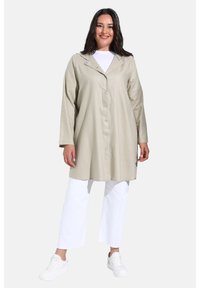 Manteau longs à boutons de couleur beige clair avec col, doté de longues manches et d'une coupe droite. Assorti à un pantalon blanc et des baskets blanches.