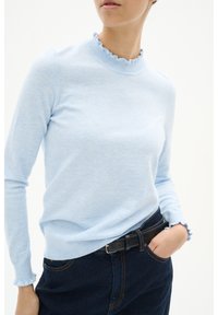 Light blue long-sleeve sweater with a ribbed, ruffled collar and cuffs, made of soft fabric. Paired with dark denim jeans and a black belt.