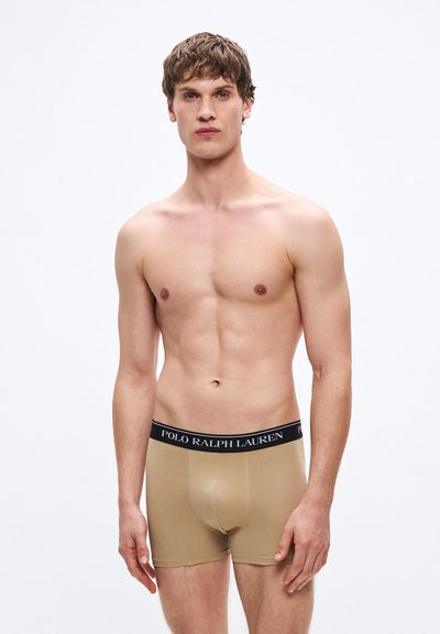 Bézs boxer alsónadrág fekete derékpánttal, amelyen a "POLO RALPH LAUREN" logó található. Sima anyag, testhezálló kialakítás, középcomb hosszúságú.