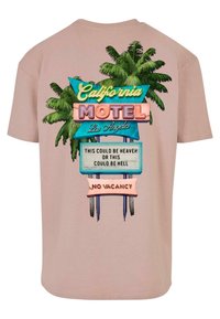 Hellrosa Kurzarm-T-Shirt mit einem bunten Grafikdesign eines Motel-Schildes, umgeben von Palmen, Text und einem dekorativen Banner mit der Aufschrift "Keine Zimmer frei".