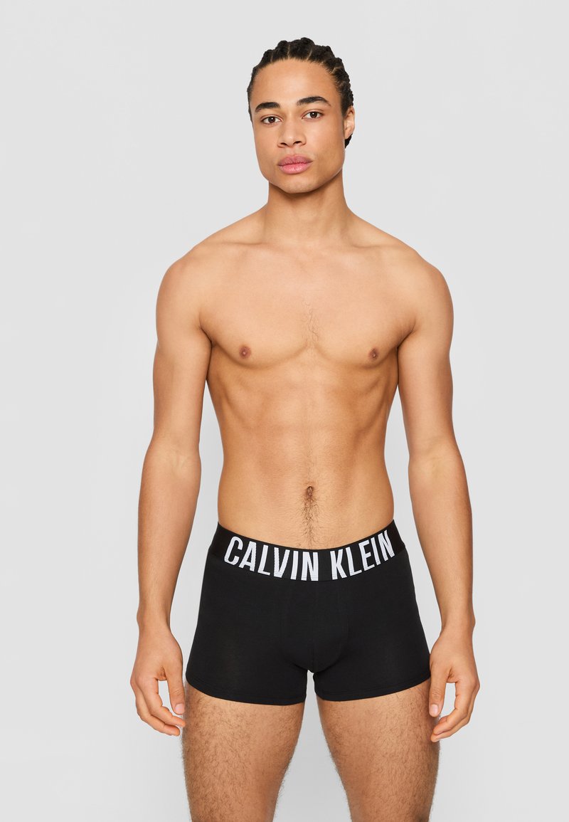 Black boxer briefs with a white "CALVIN KLEIN" logo on the elastic waistband, made of a smooth fabric, worn by a male model.