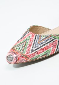 Chaussure plate pointue avec des motifs colorés, texturés en zigzag et géométriques en rouge, vert, gris, orange et noir sur la surface supérieure.